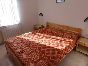 A bedroom with a wooden bed, a nightstand, a bedside table, a radiator, and a window with curtains. - Apartment Bolko (Medulin)