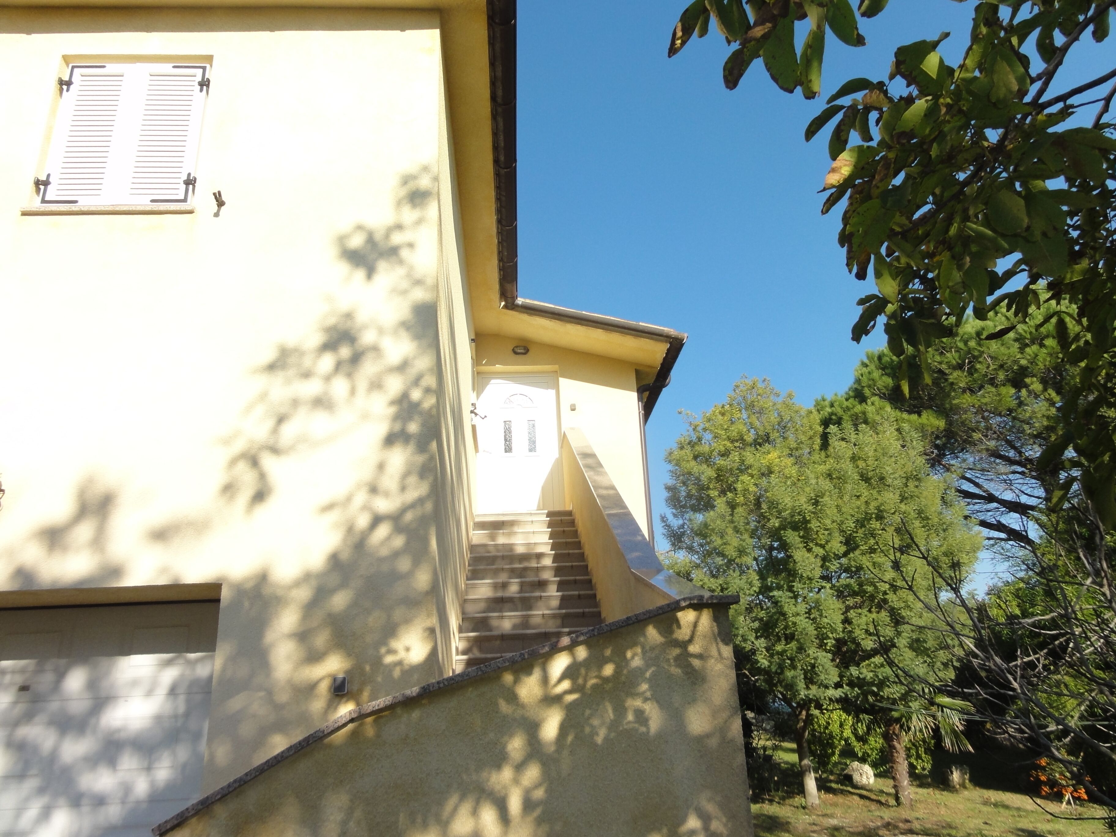 A building with a staircase leading to a door, surrounded by trees.
