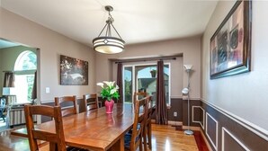 Un coin repas avec une table en bois, des chaises, un vase de fleurs, un luminaire suspendu et une vue à travers une porte vitrée.