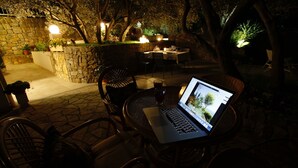 An outdoor patio with stone walls, a laptop on a table, and chairs. - Charming house with oversized heated pool (Baška Voda)