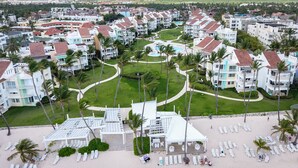 A resort with multiple buildings, a central pool, and a beach area with sun loungers. - Playa Turquesa - B-302 -Premier Beachfront Ocean View 400mbps Wifi &Free Netflix (Punta Cana)