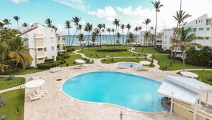A resort with a large pool, palm trees, and a view of the ocean. - Playa Turquesa - B-302 -Premier Beachfront Ocean View 400mbps Wifi &Free Netflix (Punta Cana)