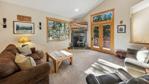 A cozy living room with a fireplace, large windows, and a ceiling fan. - Luxury Mountain Escape: BBQ, Forested, Balcony (South Lake Tahoe)