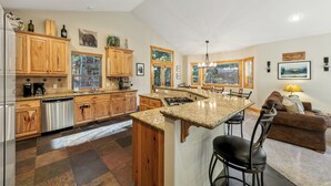 A spacious kitchen with wooden cabinets, granite countertops, and a central island. There is a dining area with a bar stool and a brown sofa. - Luxury Mountain Escape: BBQ, Forested, Balcony (South Lake Tahoe)