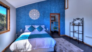 A bedroom with a large bed, a decorative wall piece, a built-in wardrobe, and a metal shelf unit. - Mayakitana - Freycinet Holiday Houses (Coles Bay)