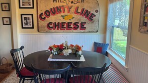 Ein Essbereich mit einem runden Tisch, schwarzen Stühlen, einer Kristallleuchtre und einem Wandzeichen mit der Aufschrift 'MILLS COUNTY LINE CHEESE'.