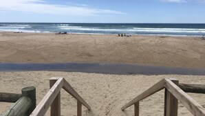 Ein Strand mit einer Holzlattenveranda im Vordergrund und Personen in der Ferne.