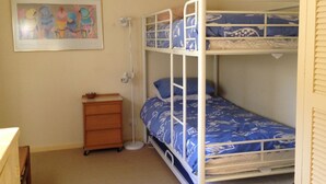 Ein Etagenbett mit blauer Musterdecke, eine Holzkommode und ein gerahmtes Bild an der Wand.