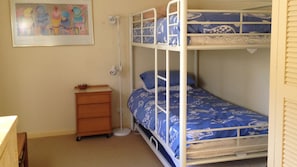 A bunk bed with a blue patterned bedspread, a wooden dresser, and a framed picture on the wall.