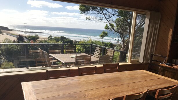 Ein Holztisch mit Stühlen, Blick auf den Ozean und ein Balkon mit Geländer.