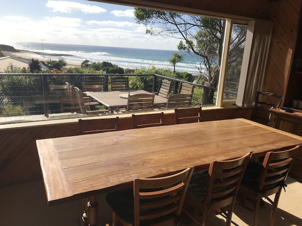 A wooden dining table with chairs, a view of the ocean, and a balcony with a railing.