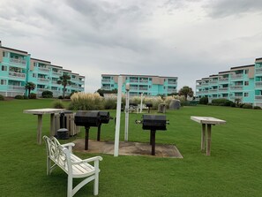 A grassy outdoor area with a white bench, barbecue grills, and a white gazebo. - Ocean-side condominium with pool. Fully-equipped for relaxed vacationing. (Atlantic Beach)