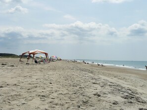 A beach with umbrellas and beach chairs, a sandy shore, and the ocean in the background. - Ocean-side condominium with pool. Fully-equipped for relaxed vacationing. (Atlantic Beach)