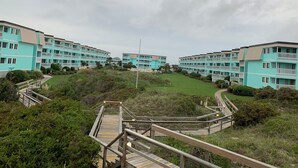 A coastal residential area with multi-story buildings, wooden walkways, and a grassy landscape. - Ocean-side condominium with pool. Fully-equipped for relaxed vacationing. (Atlantic Beach)