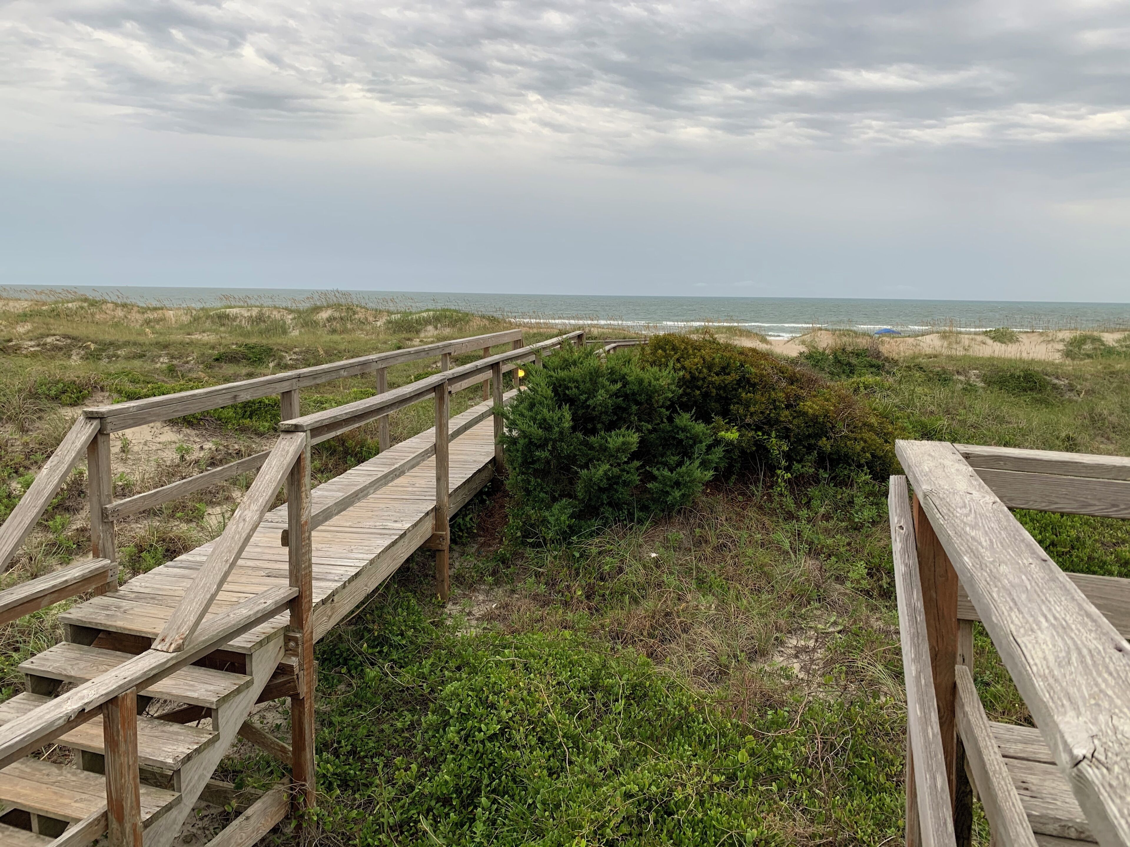Un muelle de madera que conduce a una playa con dunas y un cielo nublado.