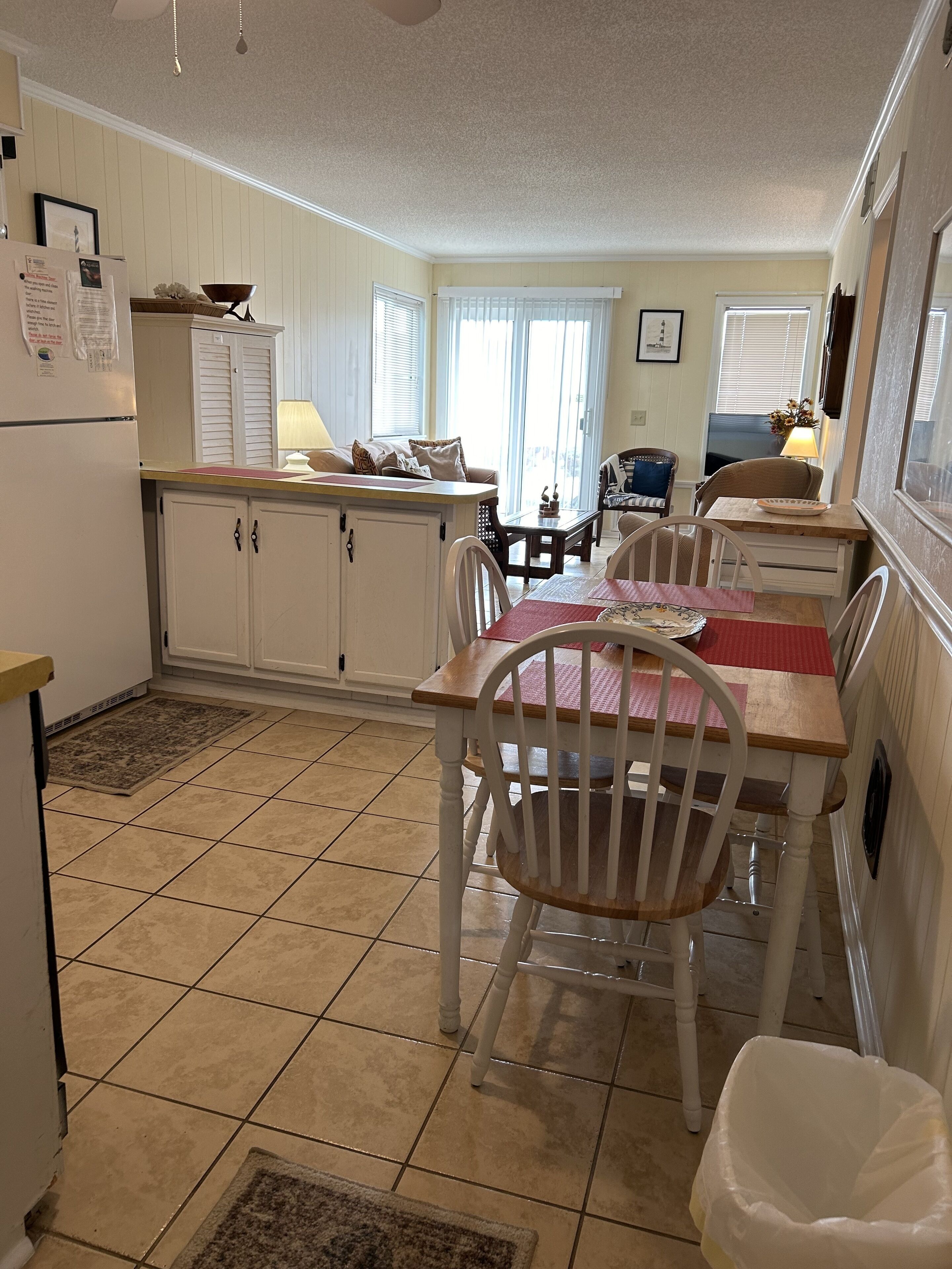 A compact kitchen with a dining area, featuring a small island, white cabinetry, and a tiled floor.