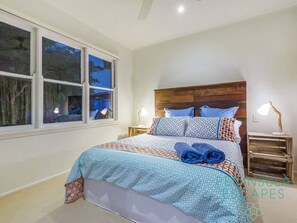 A bedroom with a large bed, a wooden headboard, and a window with a view of trees.