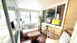 Une pièce baignée de lumière, avec un canapé, un fauteuil en osier et une lampe.