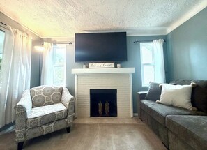 Un salon avec une cheminée, un canapé, un fauteuil à motifs et un téléviseur à écran plat fixé au-dessus de la cheminée.