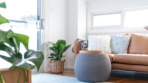 A modern living room with a wooden floor, a blue rug, a brown leather sofa, and a large window with a view. - Walk to the Beach | Live Like A Local | All The Comforts Of Home (Newcastle)