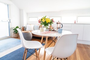 Een moderne keuken met een ronde eettafel, witte stoelen, een bloemetjesvaas en een koffiezetapparaat.