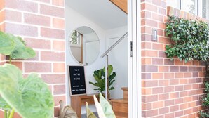 A brick building with a wooden staircase leading to a room with a mirror and a welcome sign. - Walk to the Beach | Live Like A Local | All The Comforts Of Home (Newcastle)