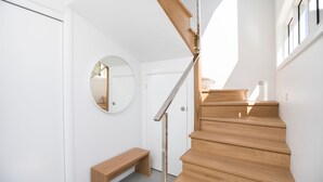 A modern staircase with wooden steps and a metal handrail, leading to a door with a round mirror on the wall. - Walk to the Beach | Live Like A Local | All The Comforts Of Home (Newcastle)