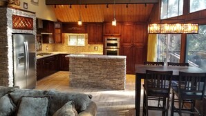 A modern kitchen with a central island, wooden cabinets, and a stone backsplash. - Surrounded by Pines, Family / Pet Friendly minutes from Snow Valley !!! (Running Springs)