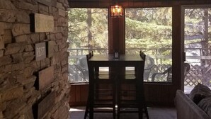 A stone wall with a table and chairs in a room with large windows overlooking a forest. - Surrounded by Pines, Family / Pet Friendly minutes from Snow Valley !!! (Running Springs)