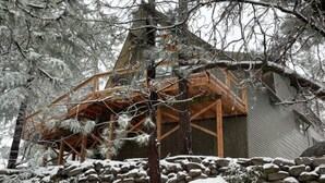 A wooden cabin with a stone foundation, surrounded by snow-covered trees. - Surrounded by Pines, Family / Pet Friendly minutes from Snow Valley !!! (Running Springs)