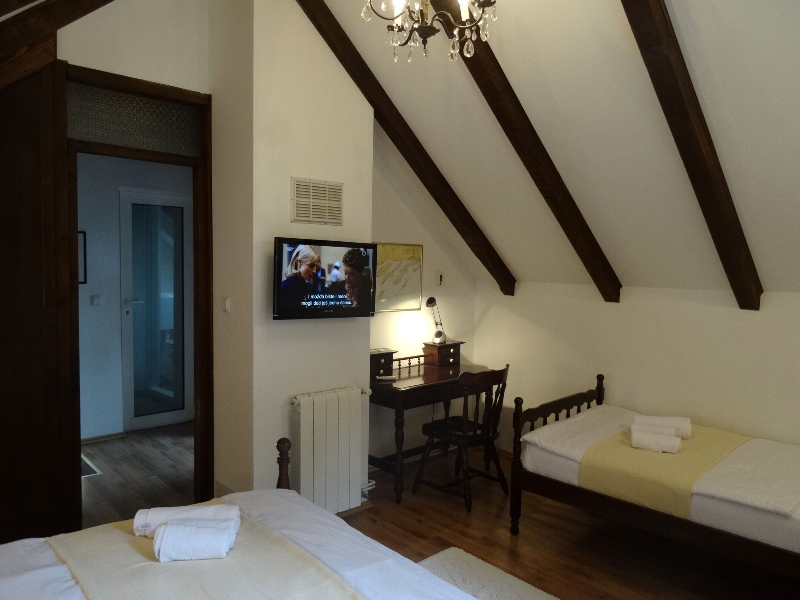 A hotel room with a bed, a desk, a chair, a television, and a chandelier.
