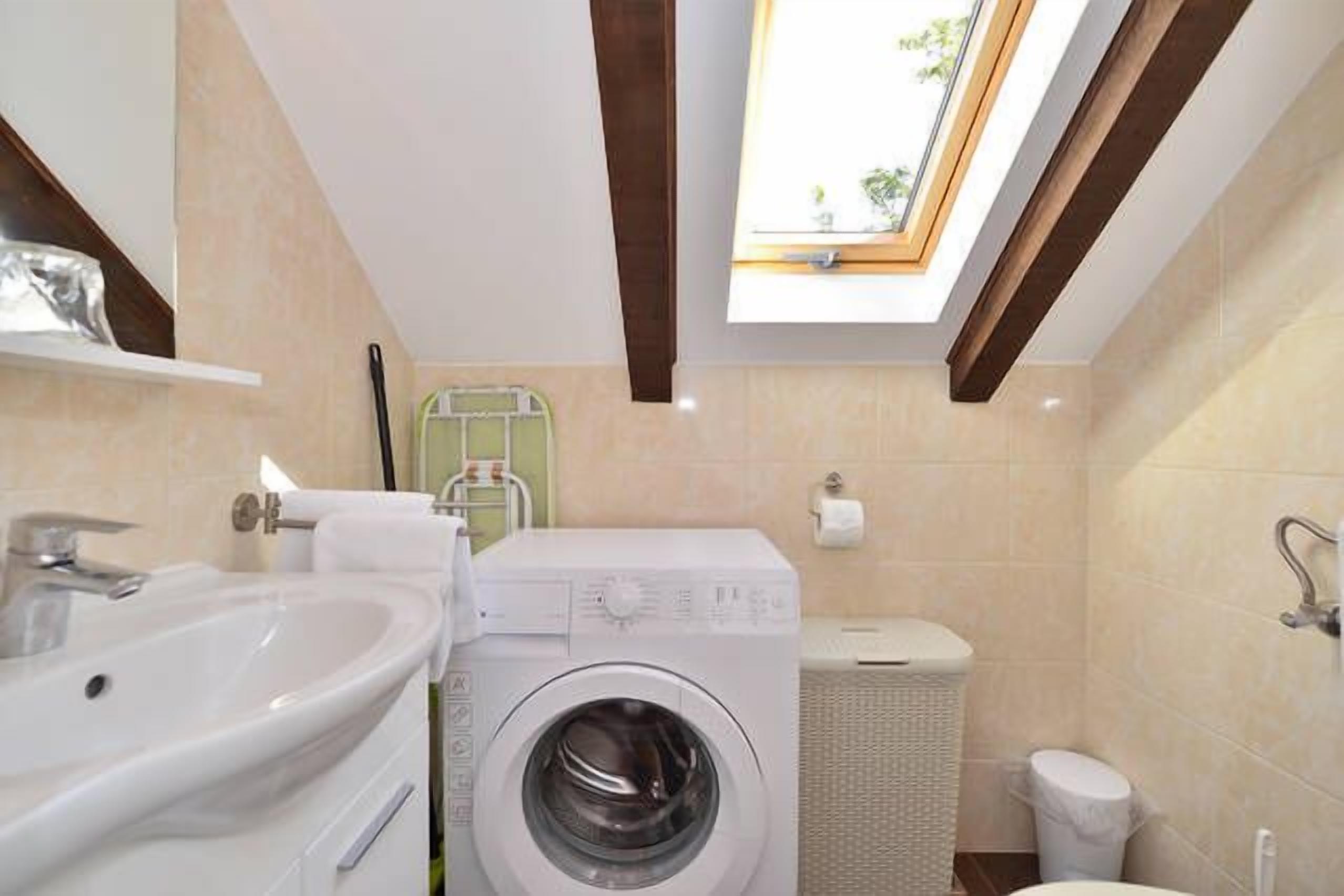 A compact bathroom with a washing machine, a sink, and a toilet.