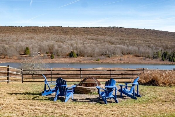 Un espacio al aire libre junto al lago con sillas Adirondack y una chimenea.
