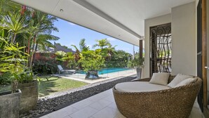 A modern outdoor living area with a pool, wicker furniture, and tropical plants. - LARASATI  @ PALM COVE (PALM COVE)