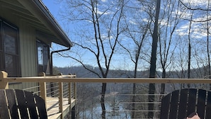 Une terrasse en bois avec deux chaises Adirondack et une rambarde donnant sur une étendue d’eau et des arbres.