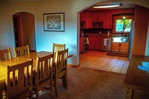 A dining area with a wooden table and chairs, a kitchen with red cabinets, and a tiled floor.