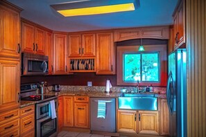 A kitchen with wooden cabinets, stainless steel appliances, a window with a view, and a ceiling light fixture.