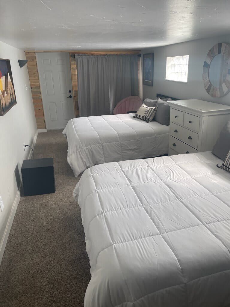 A bedroom with two beds, a dresser, a door, and a window.