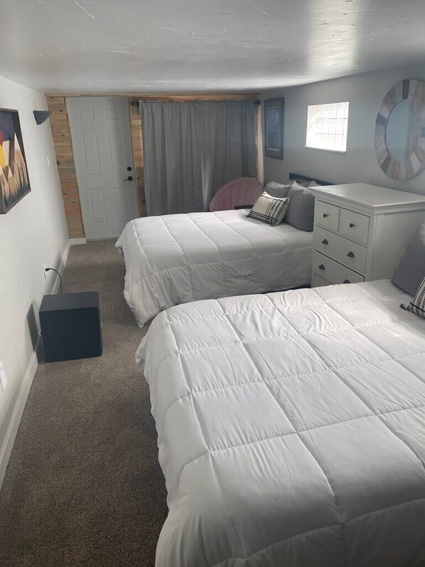 A bedroom with two beds, a dresser, a door, and a window.