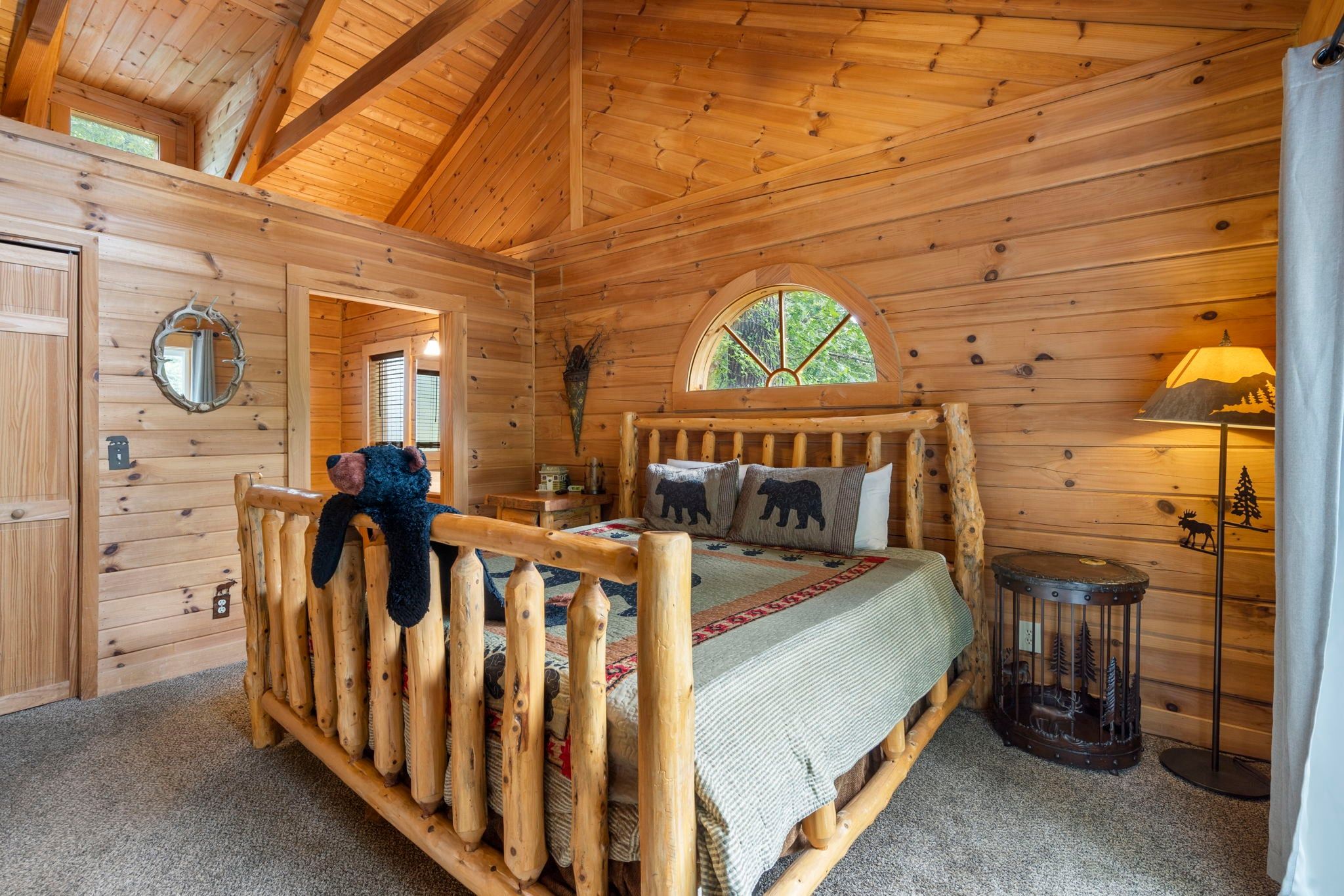 A wooden cabin bedroom with a bed, a window, a mirror, and a lamp.