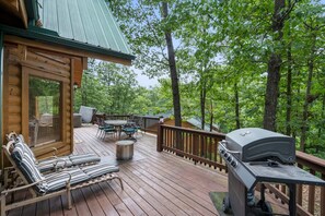 A wooden deck with outdoor furniture, a grill, and a view of the surrounding forest. - Refreshed Three Bear Log Cabin, Vaulted Ceilings, Private Hot Tub, Car Charger, Close to Big Cedar (Ridgedale)
