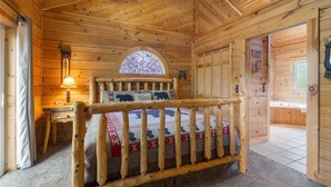 Una stanza in una baita di legno con un letto, una scrivania, una lampada e una finestra con un motivo a vetrata colorata.