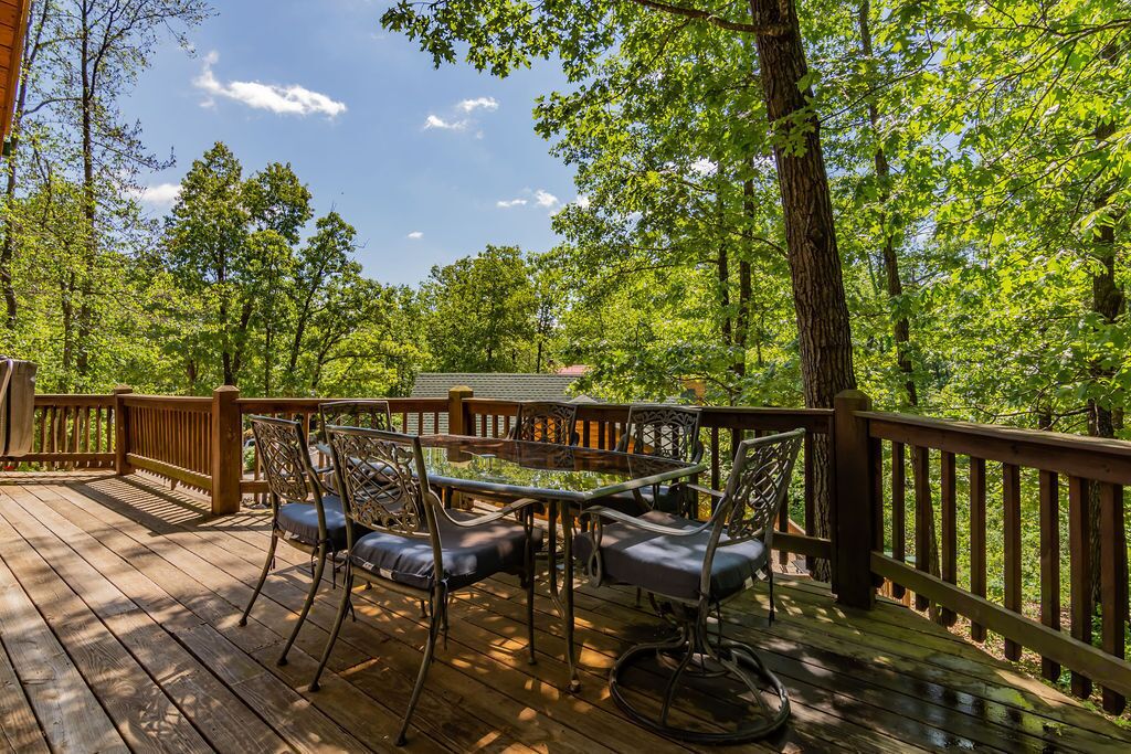 A wooden deck with outdoor furniture, surrounded by trees and a clear sky.