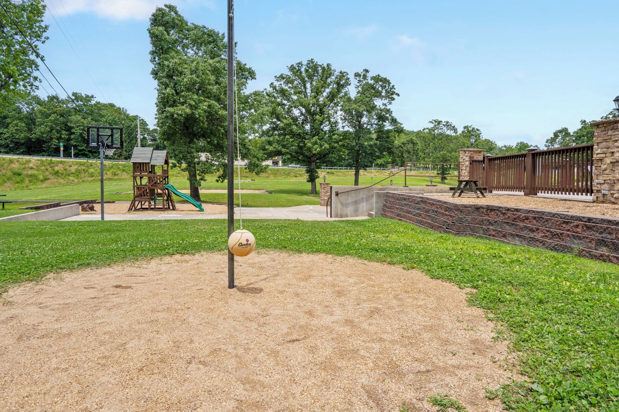 Un parque infantil con un aro de baloncesto, columpios y una pelota colgando de un poste.