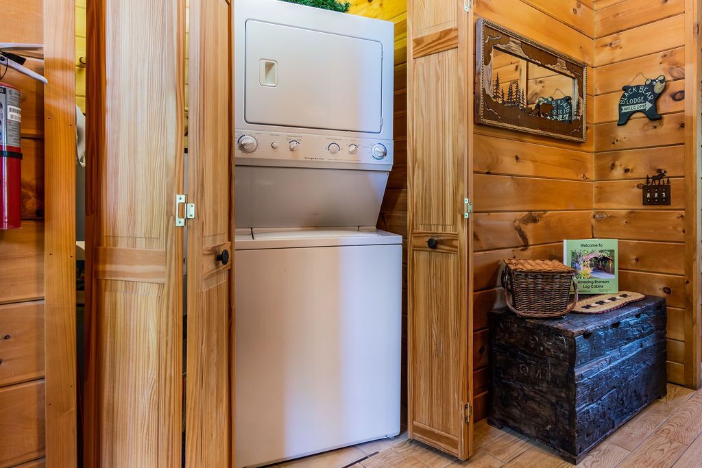 A compact room with a washing machine and dryer, wooden walls, a mirror with a scenic photo, and a welcome sign.