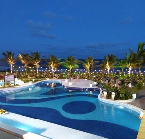 A large outdoor swimming pool with multiple sections, surrounded by palm trees and string lights.