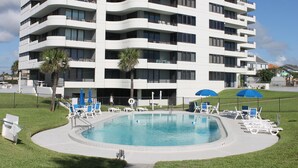 A modern multi-story hotel with a swimming pool surrounded by lounge chairs and umbrellas. - 7th Floor End Unit - Right on the Beach (Daytona Beach)