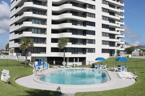 Un moderno hotel a più piani con piscina, circondata da lettini e ombrelloni.