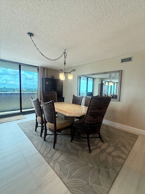 A dining area with a large table and chairs, a chandelier, and a view through large windows.
