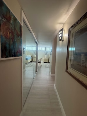 A hallway leading to a bedroom with a large window, a door, and a framed picture on the wall.